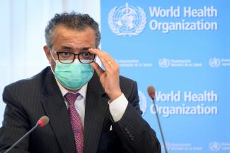 WHO Director General Dr. Tedros, pictured waering a dark suit, white shirt and purple tie, adjusts his glasses at a press conference