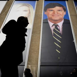 People pass by a 2-story tall promotional image of Fox News' Tucker Carlson on a building in New York, on March 13, 2019.