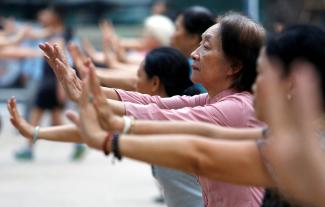Elderly people stand in a row and stretch out their arms as they exercise at a public park in Hanoi, Vietnam on October 9, 2018.