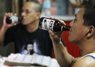 Two men are photographed from the waist up drinking beers out of the bottles at a a casual bar in the Manila metro area, in the Philippines
