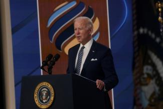 President Joe Biden delivers a speech at a podium that features the crest of the president of the United States. Biden wears a dark blue suit, white shirt and striped tie. Biden delivers remarks at the State Department's virtual Summit for Democracy, at the White House in Washington, DC, December 2021.