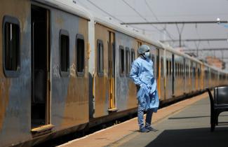 a health-care worker wearing blue scrubs and PPE stands in front of a train