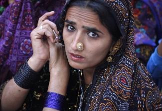 a portrait of young woman with black eyeliner and a large, gold, nose ring wearing a heavily embellished purple head scarf