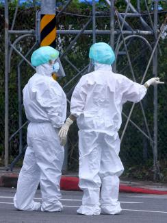 Two medical workers in full PPE talk to each other at a newly open drive-through COVID test venue in Taipei, Taiwan, on May 4, 2022.