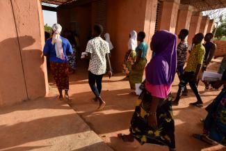 students wearing colorful clothing enter a terracotta colored building in Kenya