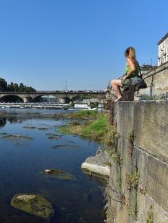 A woman sits next to Po's dry riverbed, as parts of Italy's longest river have dried up due to the worst drought in the last 70 years, in Turin, Italy, on July 15, 2022.