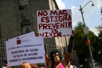 An activist wearing a monkey mask holds a white sign with painted red letters that reads, “No more stigma, preventing is living" in Spanish during a protest to call for a stronger response to the monkeypox crisis in Mexico City, Mexico, on July 26, 2022. 