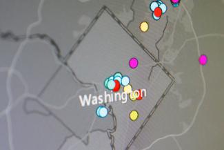 A gray topical map of washington, dc, with multicolored dots showing overdose sites in on digital dispaly