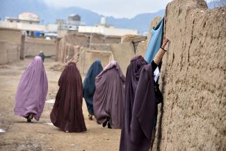 Women in lavender, blue, and burgundy burqas who are part of an immunization team write a message on the wall of a stone house during a vaccination campaign in Kandahar, Afghanistan, on January 28, 2020. 