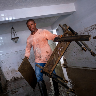 A young man in rain boots, jeans, and a long-sleeved t-shirt wades through knee-deep water in his home, carrying damaged furniture in the aftermath of Hurricane Fiona, in Toa Baja, Puerto Rico, on September 20, 2022. 