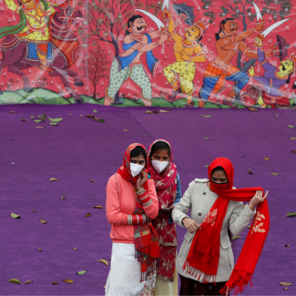 Women wearing protective face masks and colorful red and white saris stand in front of a purple wall and a color mural as they watch a dress rehearsal for the Republic Day parade, in New Delhi, India, on January 23, 2022. REUTERS/Adnan Abidi