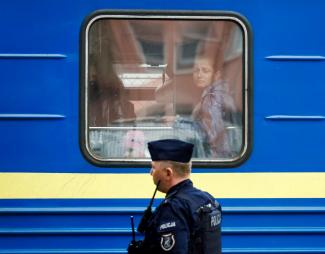 Ukrainian refugees look out of a window on a train arriving from Odesa after crossing the Ukraine-Poland border, amid the Russian invasion of Ukraine, as a Polish police officer keeps watch at Przemysl Glowny train station in Przemysl, Poland, April 21, 2022.