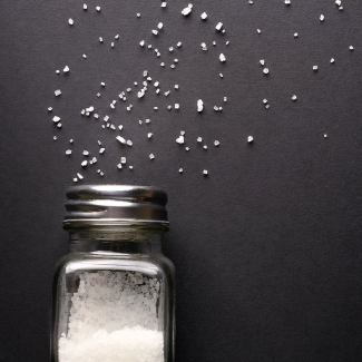 White sea salt spills from a glass salt shaker onto a black table. 