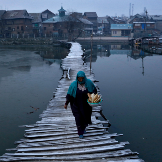 A woman dressed in a head covering and long dress carries bread as she walks on a frost-covered footbridge in the interiors of Nigeen Lake on a cold winter morning in Srinagar, India, December 24, 2020. REUTERS/Danish Ismail