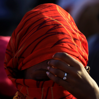 A close-up photo of an Ethiopian woman wearing a read head scarf with her hand held to her forehead. She fled the ongoing fighting in Tigray, in Hamdayet village near the Sudan-Ethiopia border, in Kassala State, Sudan, on November 22, 2020. 