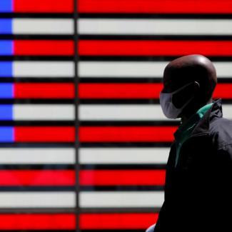 A giant red, white, and blue lit-up U.S. flag can be seen behind a person wearing a mask while walking in Times Square after the CDC announced new guidelines regarding outdoor mask wearing and vaccination during the COVID outbreak in New York City, New York, on April 27, 2021. 
