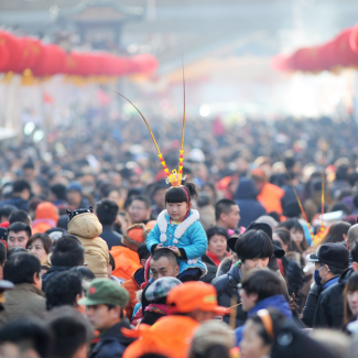 A girl wears a monkey king headwear as she sits on an adult's shoulders in a huge crowd at a festival fair during Chinese Lunar New Year celebrations in Qingdao.