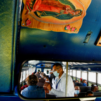 A rearview mirroron a bus reflects the image of assembly factory employees sitting in the bus waiting to receive COVID-19 vaccines. A health worker in a white medical coat is giving a vaccine to one of the women. Photo taken in Ciudad Juarez, Mexico, on May 24, 2021. 