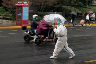 A worker in a white, protective suit holding an umbrella crosses a road in the rain during a COVID-19 outbreak in Shanghai, China, November 30, 2022.