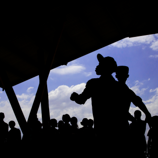 The silhouettes of teens are seen against a blue sky with white clouds and a dark roof on the left side of the image