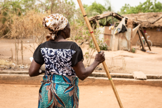 Agnes Kalié, a health worker, holds a long stick as she stands near on a dirt road. She dispenses medication to people to prevent neglected tropical diseases in Nigeria. 