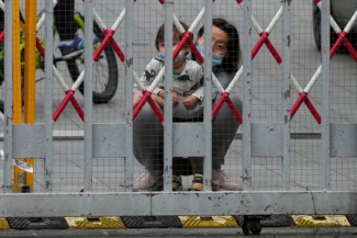 A resident and a child look out through gaps in barriers at a closed residential area during COVID-19 lockdown in Shanghai, China, on May 10, 2022. 