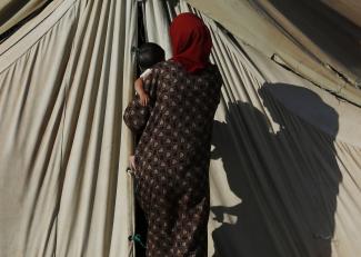 A Syrian refugee from Damascus carries a child as she enters her tent at the Majdal Anjar refugee camp in Bekaa Valley near the Syrian border in eastern Lebanon, on September 9, 2013.