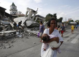 A woman carries her baby past a destroyed church belfry, in Tubigon, Bohol, a day after an earthquake hit the central Philippines, on October 16, 2013.
