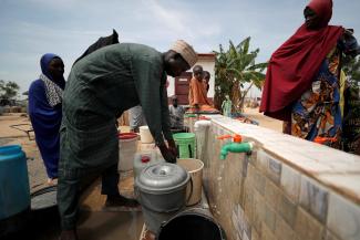 A community health worker adds chlorine to water while internally displaced people gather to fill their buckets at the water point in Muna Garage IDP camp in Maiduguri, Borno State, Nigeria, on October 23, 2022.