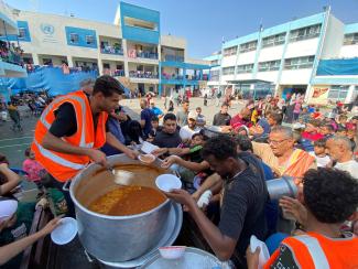 Palestinians, who fled their houses due to Israeli strikes, gather to get their share of charity food offered by volunteers