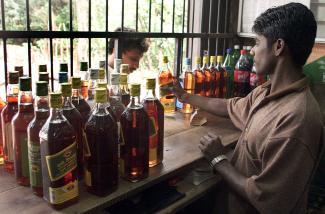 A man of South Asia descent stands at a counter selling bottles of liquor. 