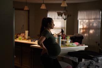 A pregnant woman stands in her kitchen. 