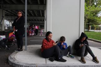 A group of kids on smartphones sit on the sidewalk.