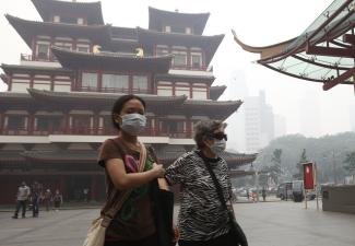 An elderly woman in face mask is accompanied by a helper.