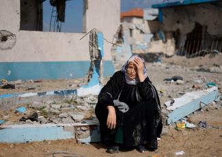 A woman rests next to a damaged building, as Palestinian arrive in Rafah after they were evacuated from Nasser hospital in Khan Younis.