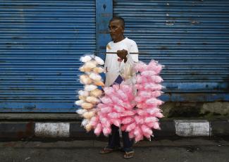 A vendor selling candy floss stands in front of closed shops along the roadside.