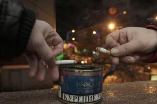 Men tap ash from their cigarettes while smoking on the balcony of an office building.