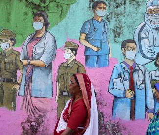 Women walk past a COVID-19 themed mural on the street.