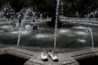 The tennis shoes rest on a fountain during a heat wave.