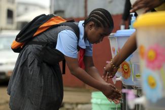 A pupil washes her hands with an improvised tap in front of a school.