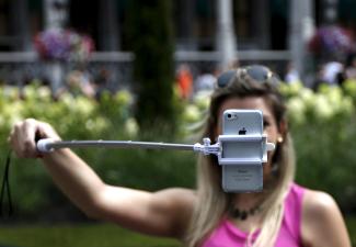 A tourist uses a selfie stick to take a photograph near a floral display.