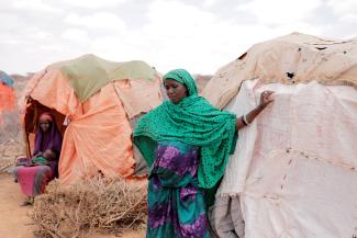 A pregnant displaced woman stands beside her shelter at a makeshift settlement.