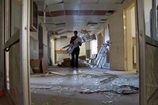 A man carries crutches as he walks on glass fragments inside a damaged hospital after what activists said were barrel bombs dropped by forces loyal to Syria's President Bashar al-Assad and fell near the hospital in the town of Tel al-Shehab in Deraa, Syria July 23, 2015.
