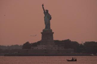 The Statue of Liberty is seen at sunset through haze caused by smoke from Canadian wildfires, as viewed from Brooklyn, New York, August 5, 2025.