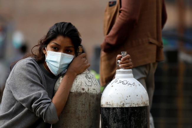 a young woman wearing a light blue surgical face mask rests her head on an empty oxygen tank
